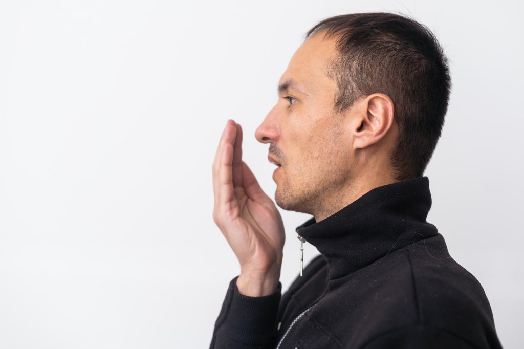 Man checks his breath with his hand. The concept of halitosis.