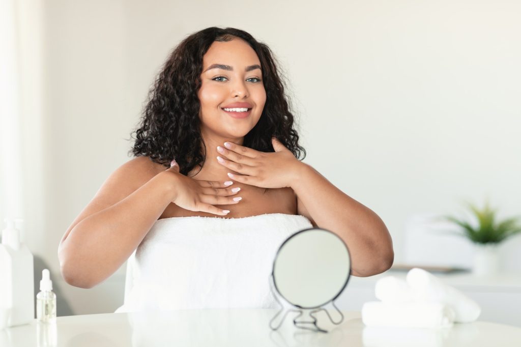 Perfect healthy skin. Happy body positive woman in towel applying moisturizing cream on her neck